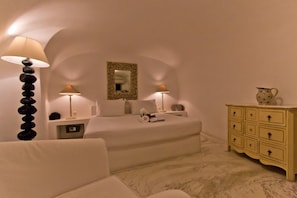 A bedroom with a bed, two bedside lamps, a nightstand, a dresser, and a wall-mounted mirror. - Onar Villas Oia - Onar Hotels Collection (Santorini)