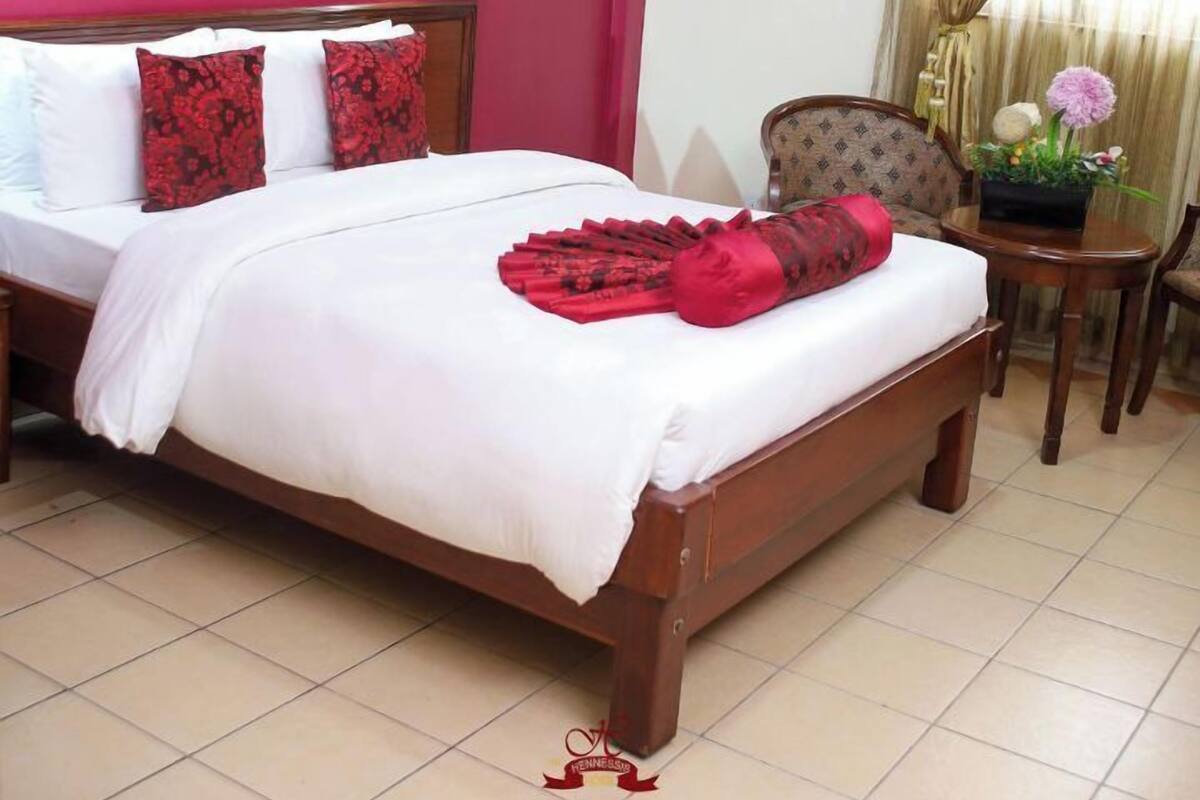 A hotel room with a wooden bed, a red wall, a framed picture, and a window with curtains.