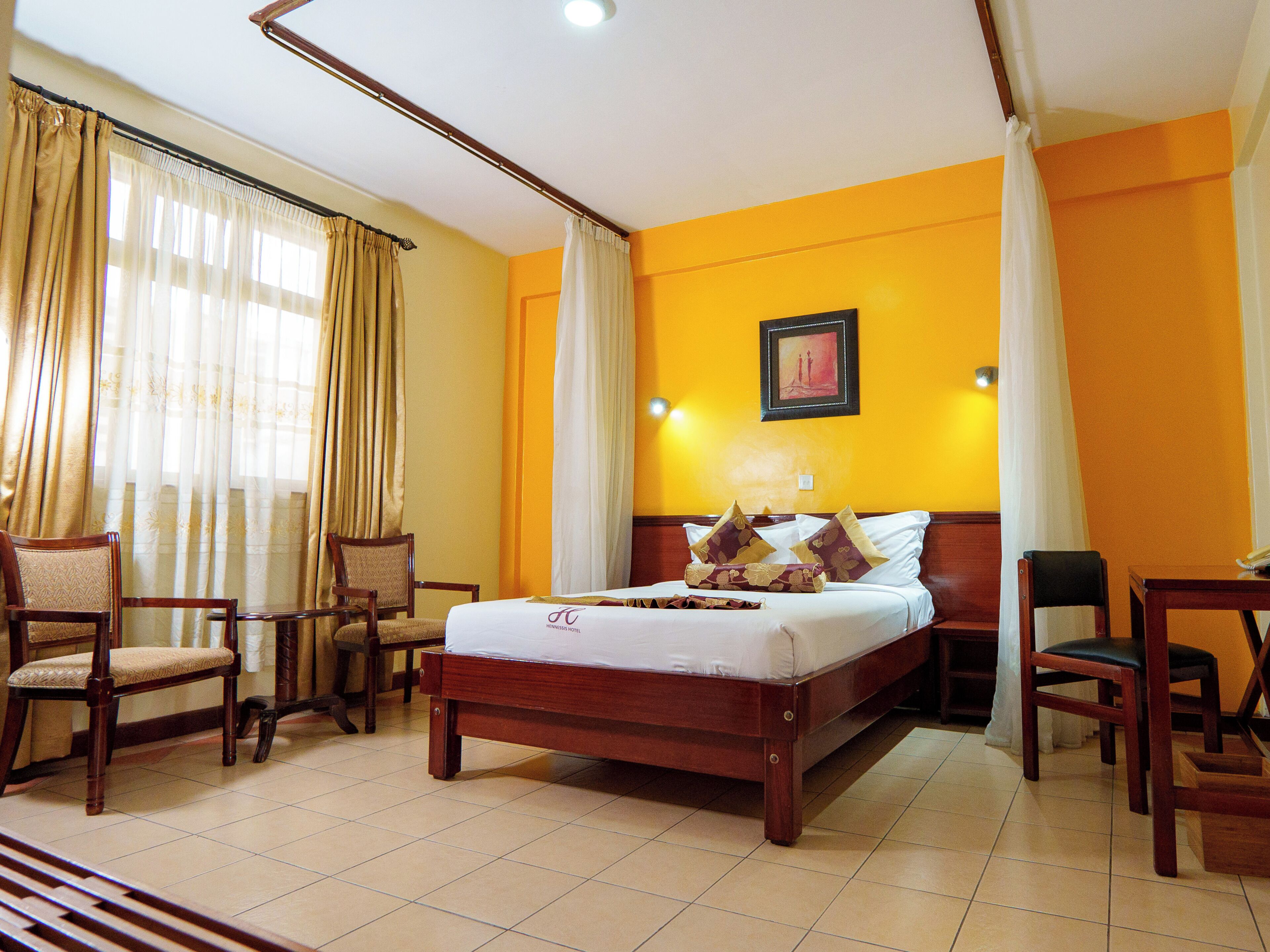 A hotel room with a bed, two chairs, a desk, and a painting on the wall.