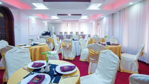 Un salón de banquetes con mesas redondas, sillas blancas y una alfombra roja.