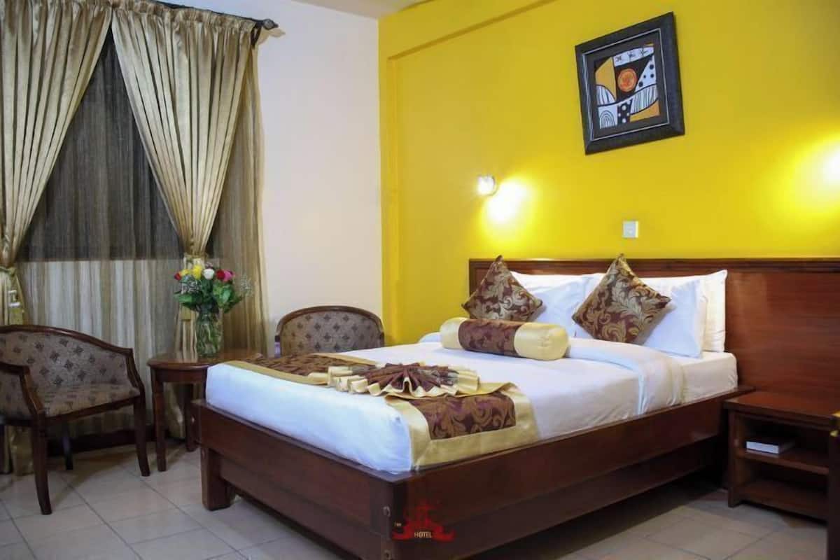 A hotel room with a wooden bed, a nightstand, a chair, and a window with curtains.