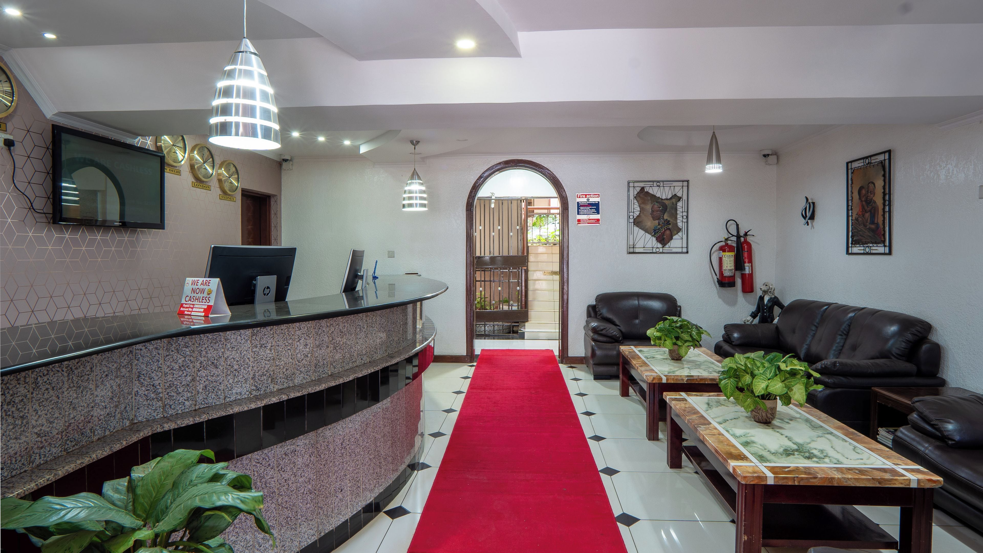A hotel lobby with a reception desk, seating area, and a red carpet leading to the exit.