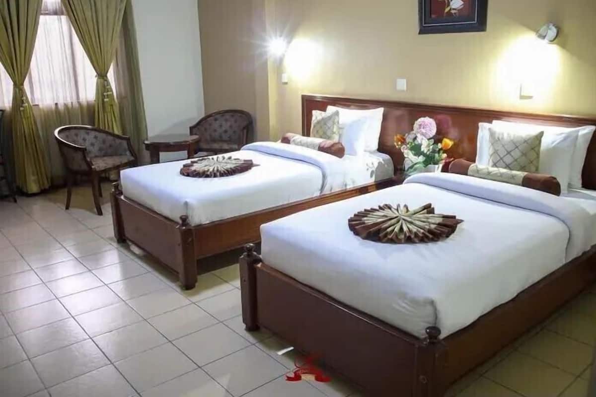 A hotel room with two single beds, a chair, a small table, and a wall-mounted clock.