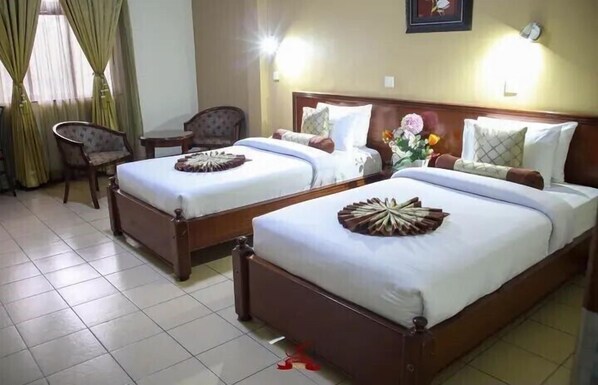 Habitación de hotel con dos camas individuales, una silla, una mesita y un reloj en la pared.