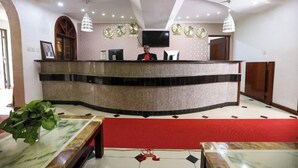 Un área de recepción con mostrador curvo, un televisor en la pared y una alfombra roja que conduce al área de descanso.