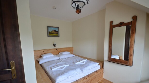 A room with a wooden bed, a wooden bench, a wall-mounted mirror, and a ceiling light fixture. - Revesz Hotel (Gyor)
