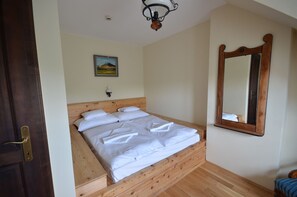 A room with a wooden bed, a wooden bench, a wall-mounted mirror, and a ceiling light fixture. - Revesz Hotel (Gyor)