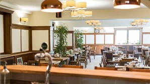 A restaurant with wooden paneling, multiple tables, and hanging chandeliers. - Revesz Hotel (Gyor)