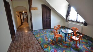A room with a sloped ceiling, a tiled floor, a colorful play mat, and a table with chairs. - Revesz Hotel (Gyor)