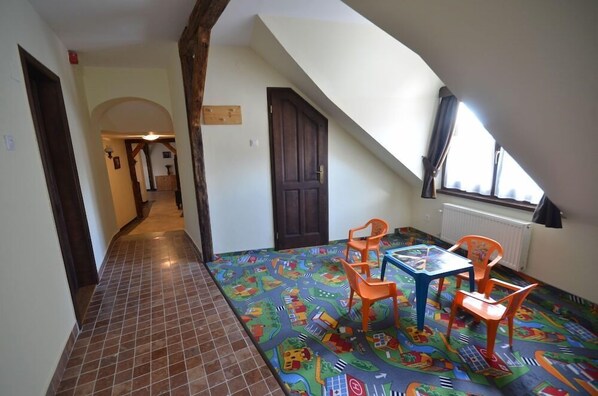 A room with a sloped ceiling, a tiled floor, a colorful play mat, and a table with chairs. - Revesz Hotel (Gyor)