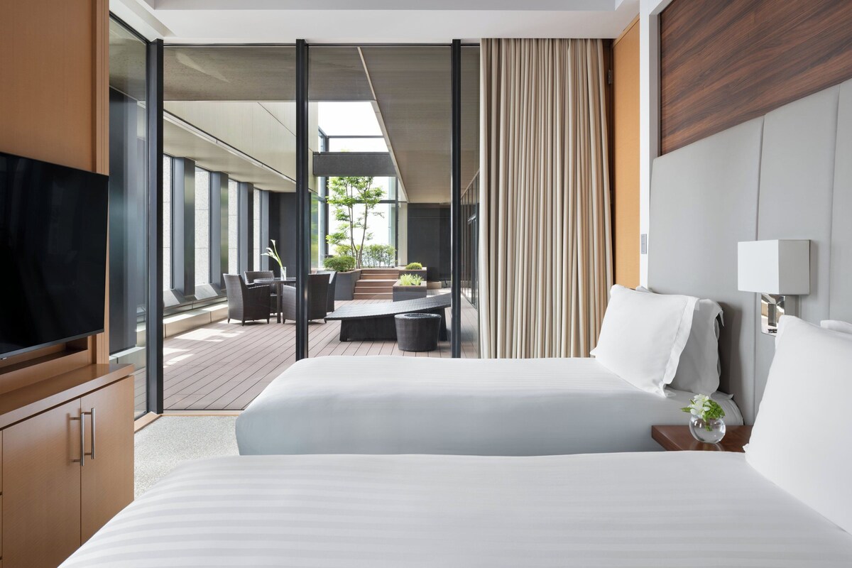 A modern hotel room with a large bed, a television, a desk, and a view of the outdoors.
