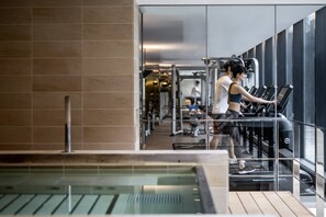 A modern gym with treadmills and exercise equipment, a glass wall, and a pool area.