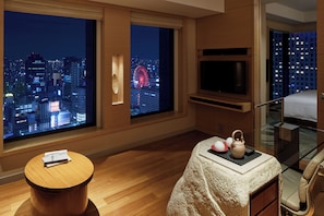 A hotel room with a large window offering a city view, a flat-screen TV, a small round table, and a bed with a glass-enclosed balcony. - InterContinental Osaka by IHG (Osaka)