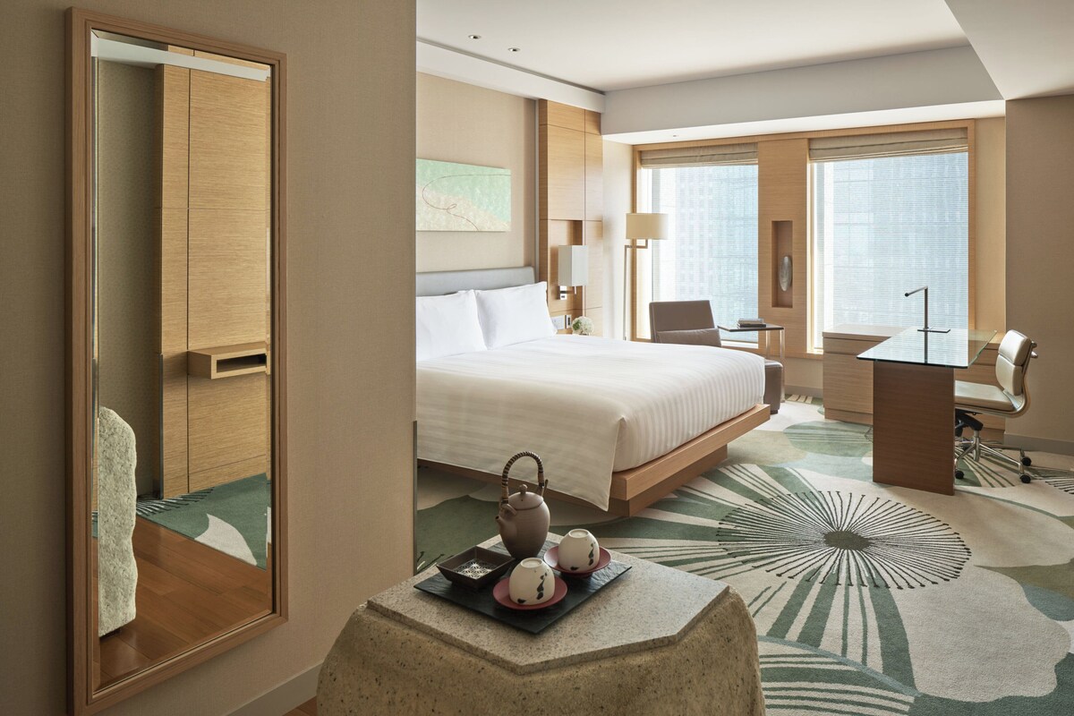A hotel room with a bed, a desk, a chair, a mirror, and a tea set on a table.
