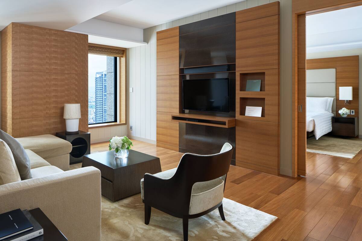 Habitació d'hotel moderna amb un televisor gran, un sofà, una taula de cafè i vistes a la ciutat.