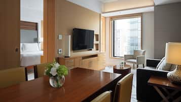 Habitación de hotel con cama, televisión, mesa de comedor con sillas, sofá y ventana con vista a la ciudad.