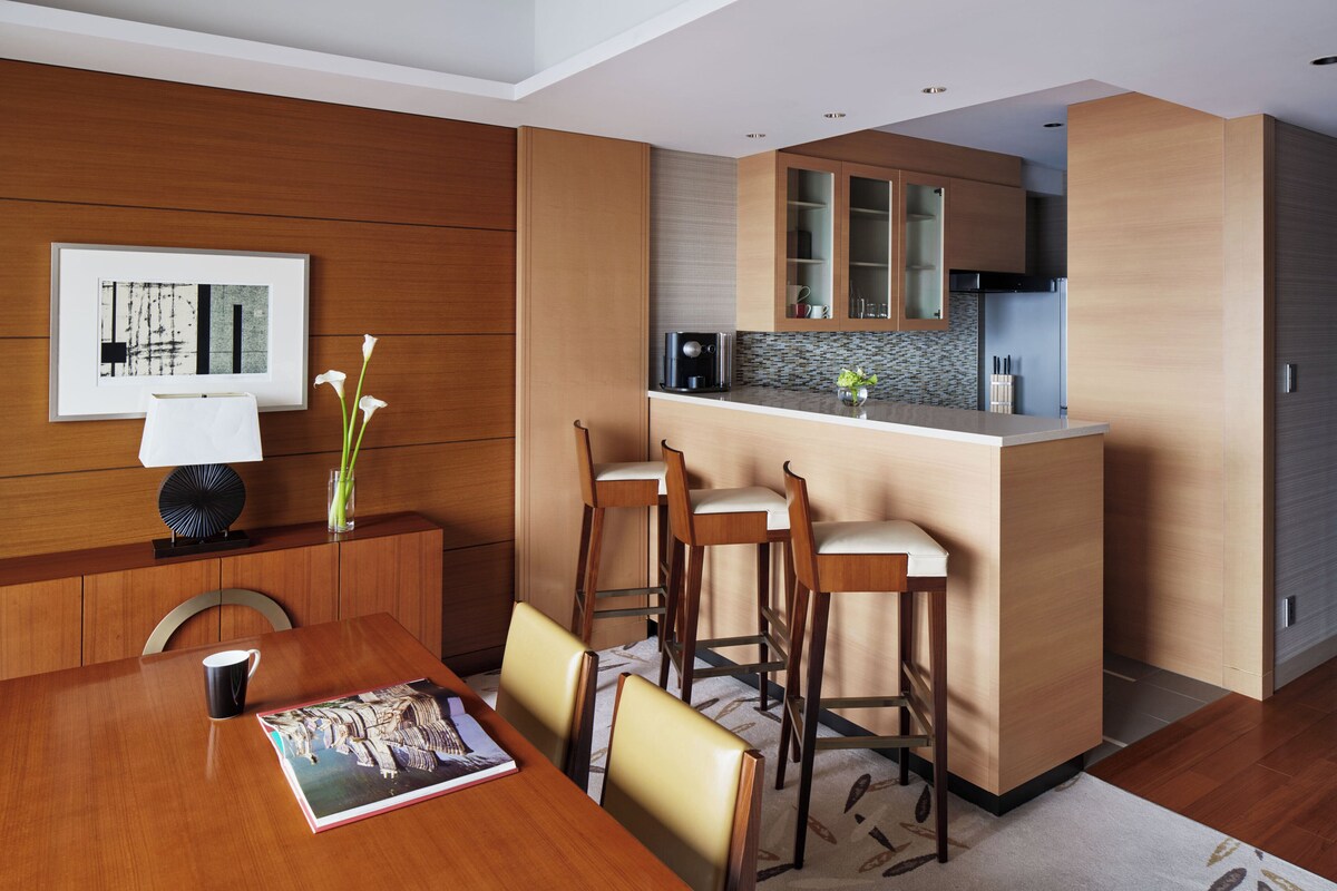 A modern kitchen with wooden cabinets, a built-in island with bar stools, and a dining area with a table and chairs.