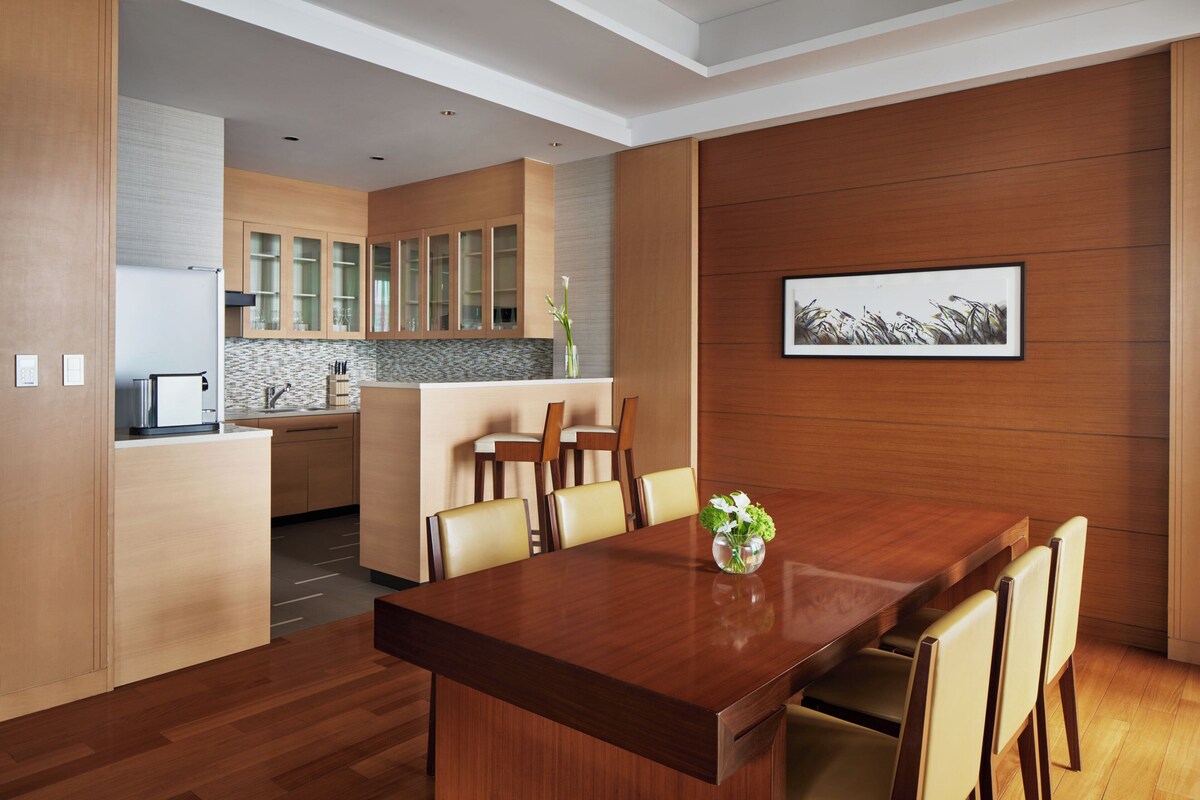 A modern kitchen with wooden cabinets, a dining area with a wooden table and chairs, and a framed picture on the wall.