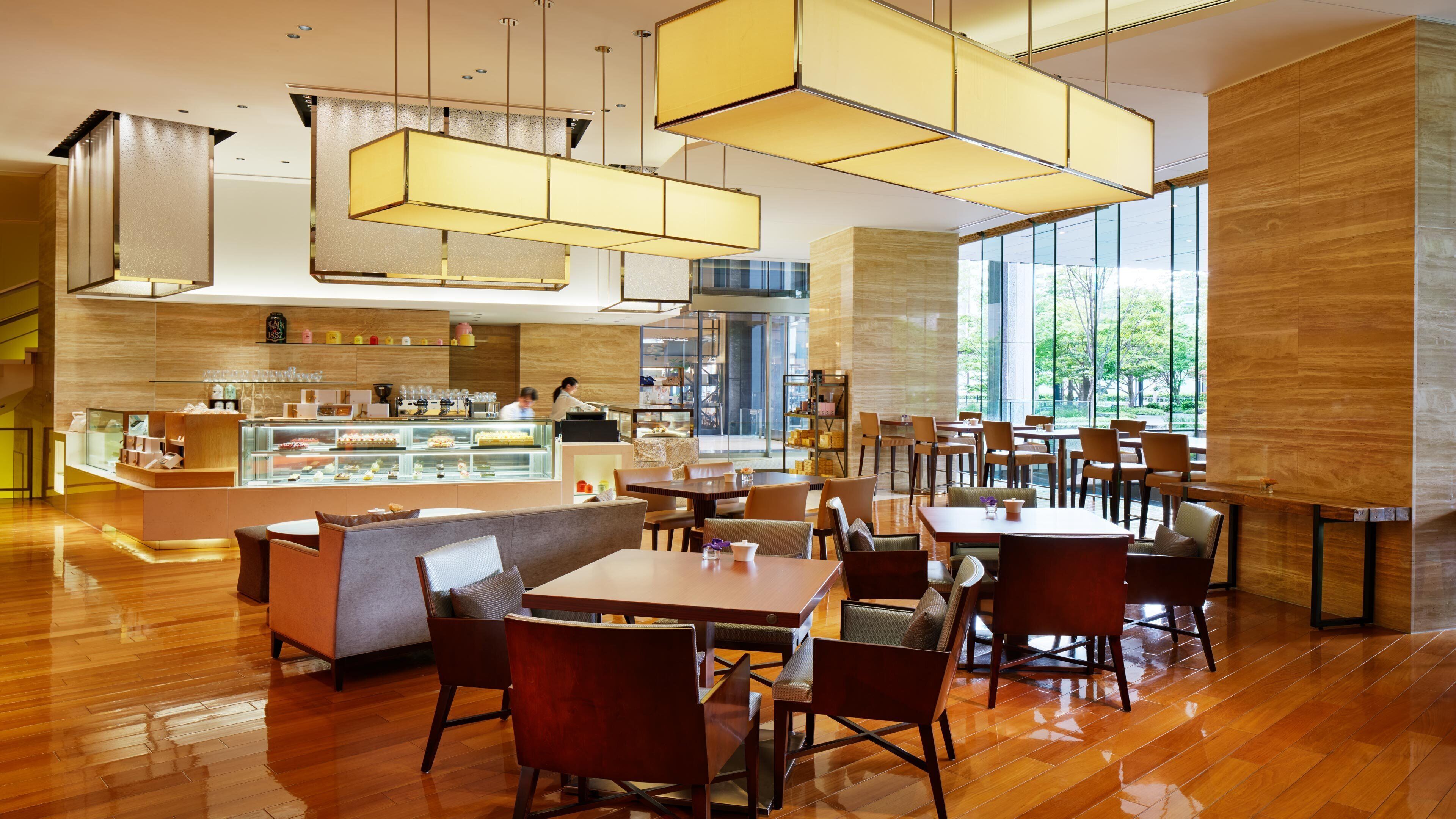 A modern restaurant with wooden flooring, multiple tables and chairs, and a dessert display.