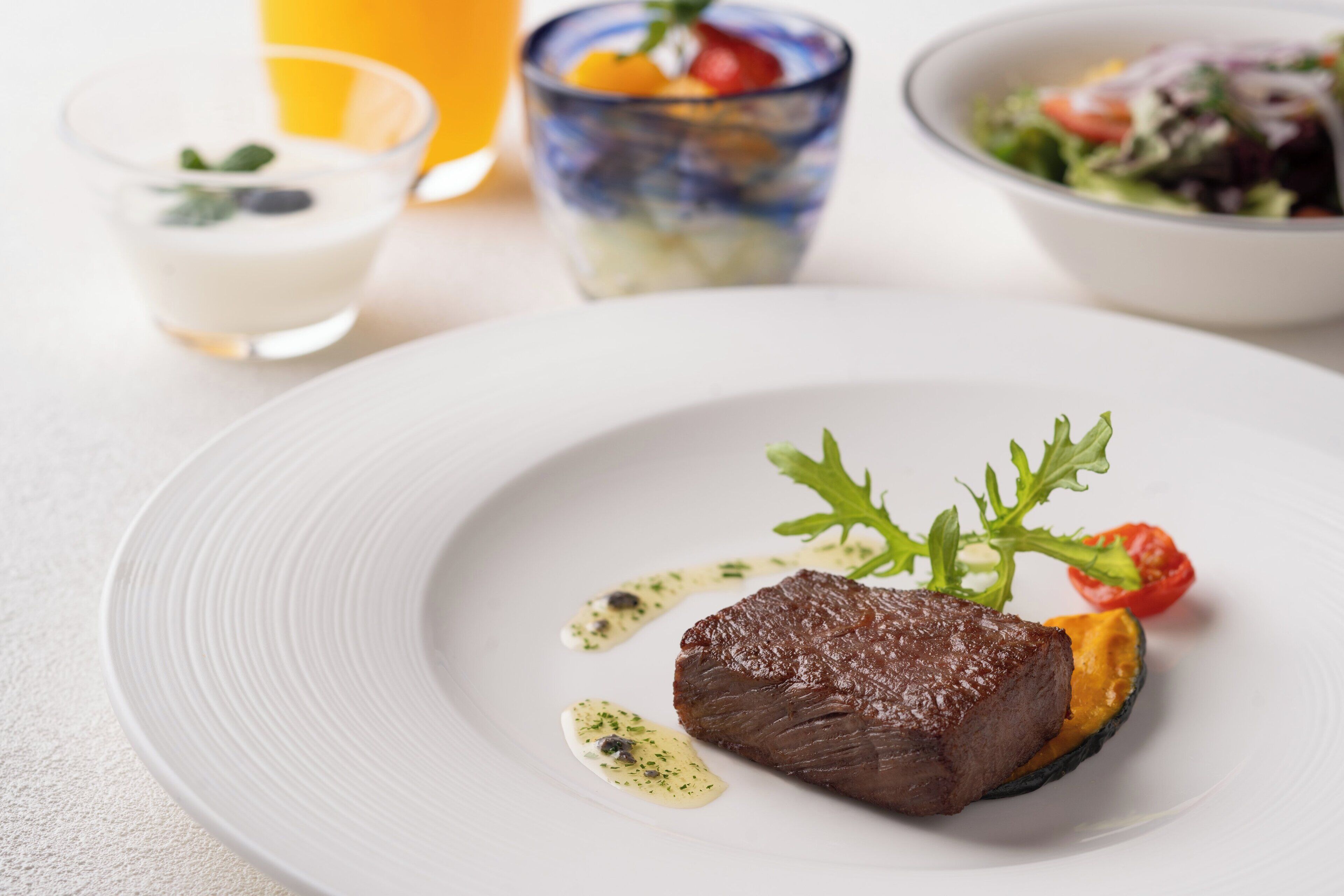 A plate with a steak, greens, and a cherry tomato.