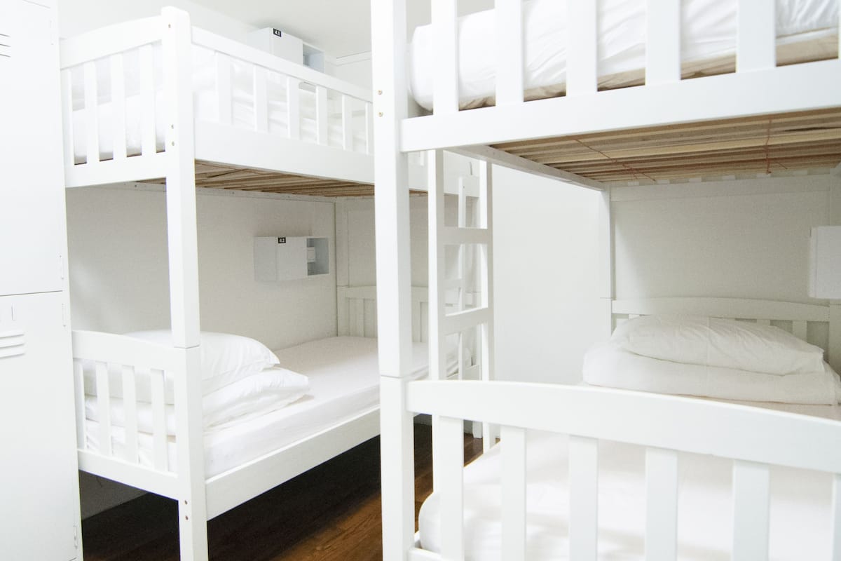 Une chambre avec un lit superposé, du linge de lit blanc et un plancher en bois.