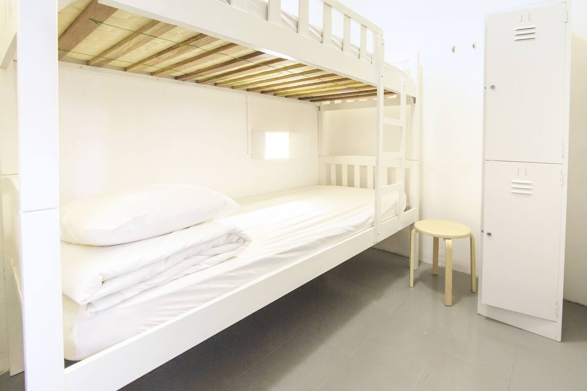 Une chambre avec un lit superposé, un petit tabouret et une armoire blanche.