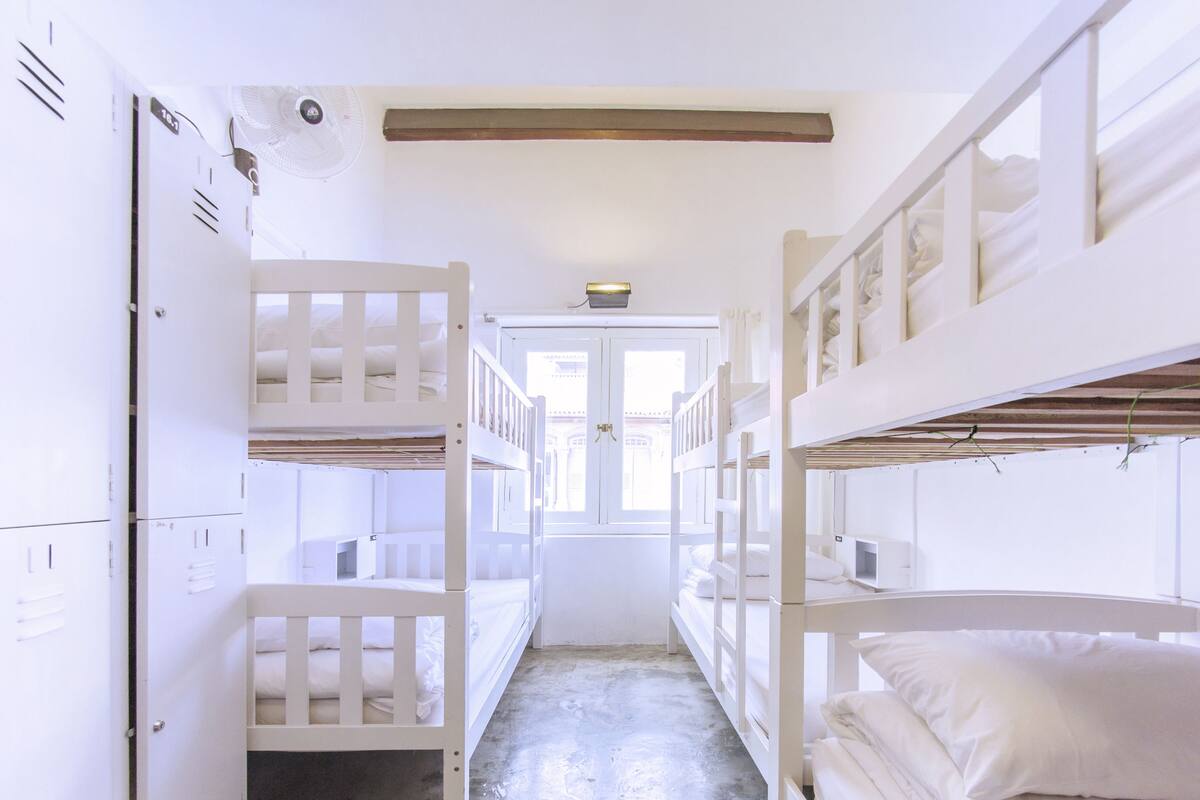 Une chambre avec des lits superposés blancs, une porte et une fenêtre.