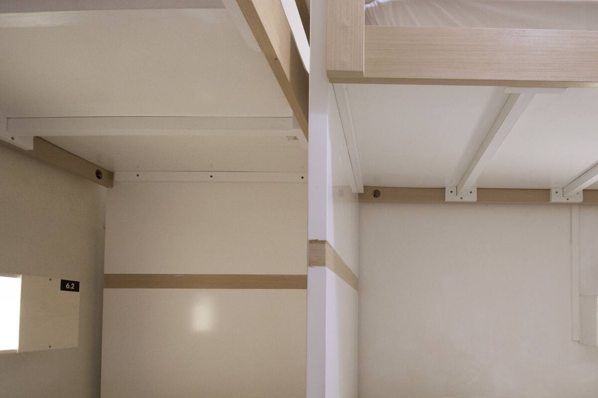 Deux lits superposés avec du linge de lit blanc, un plafond en bois et une petite fenêtre ornée d’un panneau indiquant un numéro.