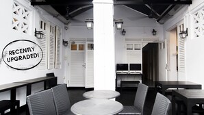 Un área de estar interior recientemente renovada con sillas y mesas de mimbre, puertas blancas y vigas de techo negras.