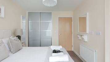 Quarto de hotel com cama, mesa de cabeceira, abajur, espelho, guarda-roupa e radiador.