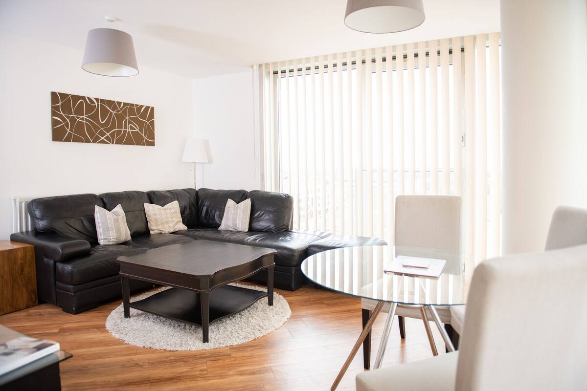 Un salon moderne avec un canapé en cuir noir, une table basse en verre et un fauteuil blanc.
