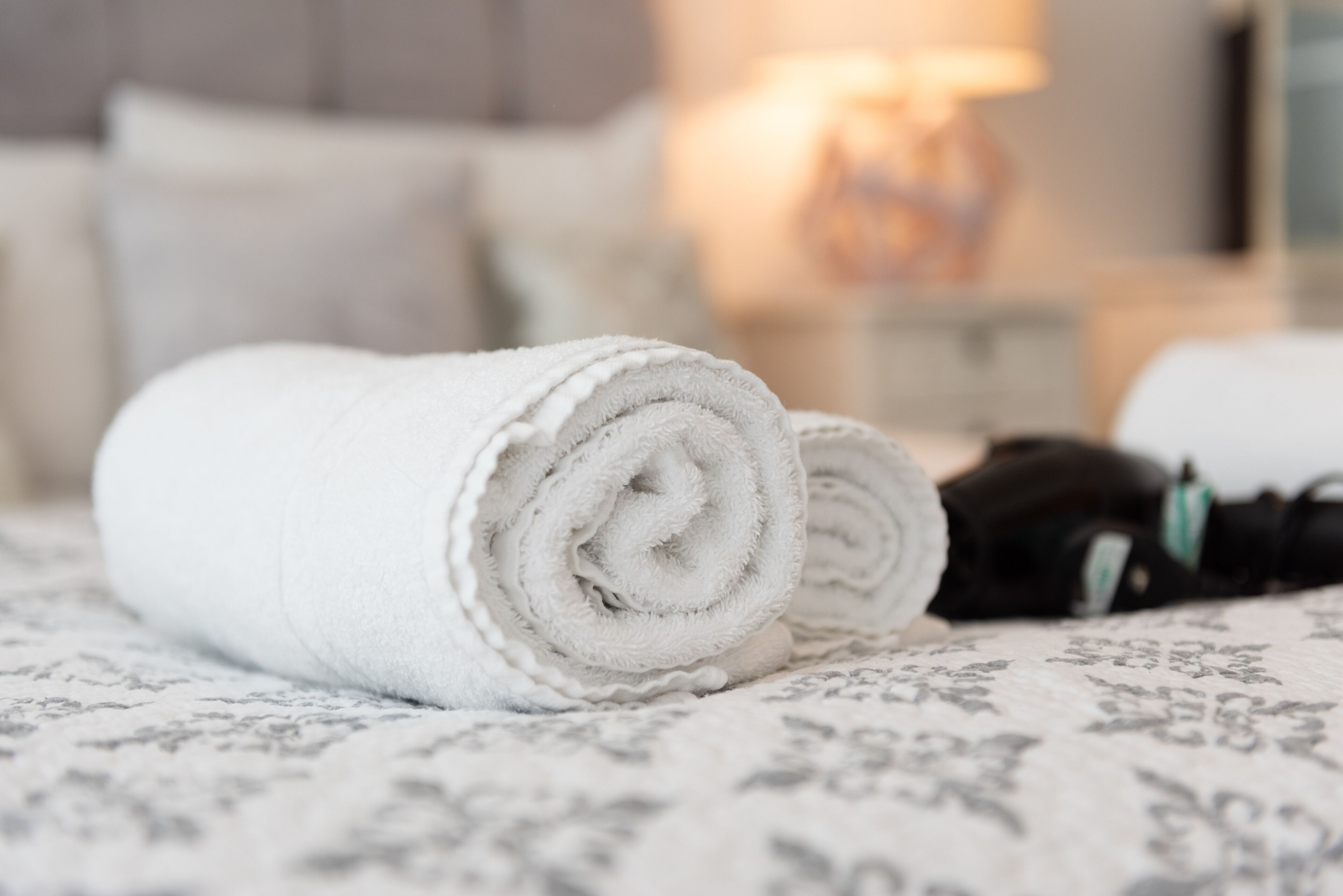 A neatly folded white towel on a bed with a patterned bedspread.