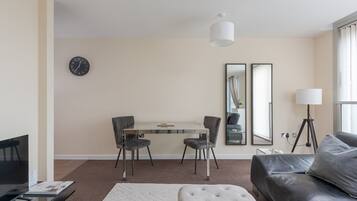 Een moderne woonkamer met een bank, een voetenbankje, een eettafel met stoelen, een televisie, een klok en twee spiegels.