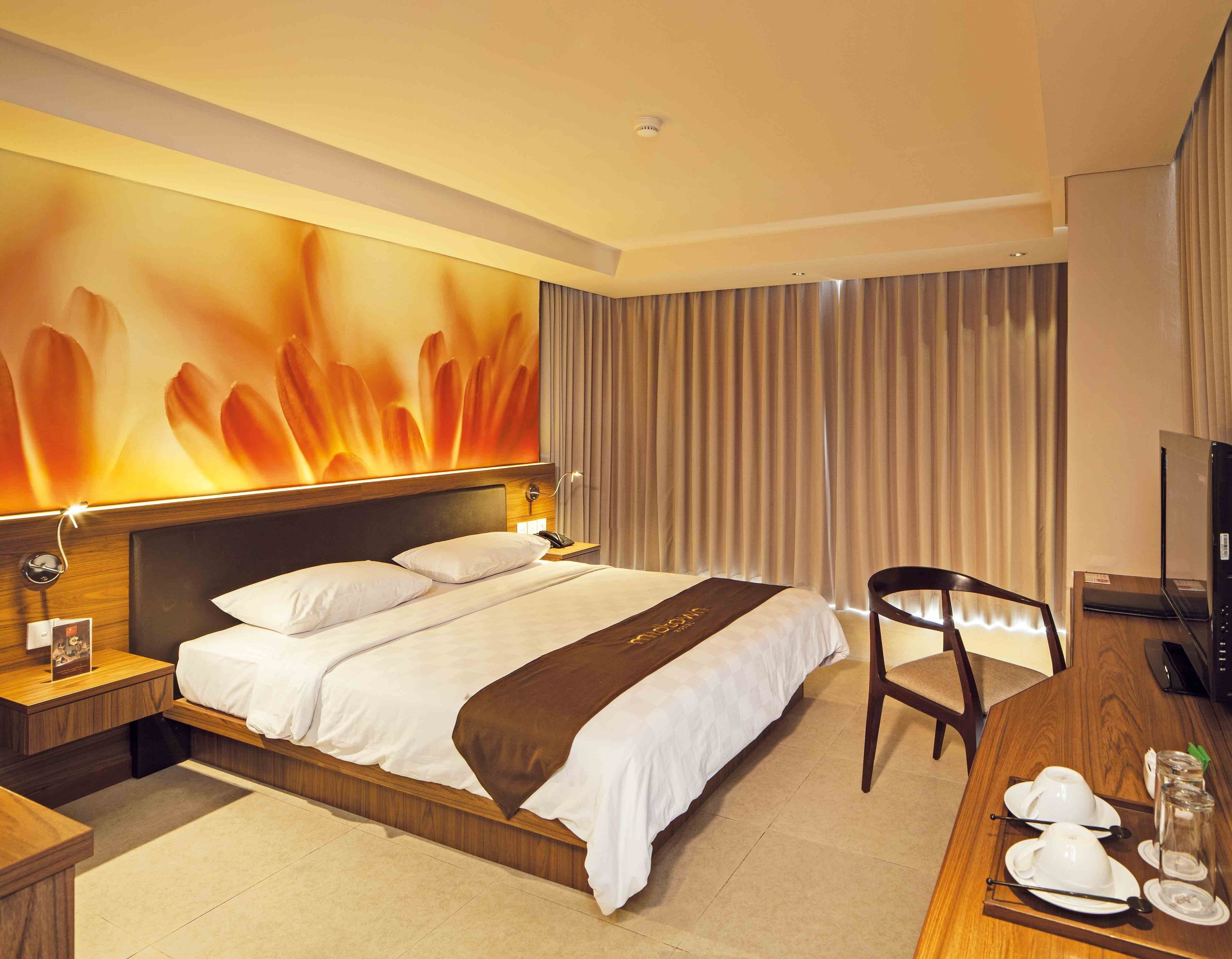 Quarto de hotel com uma cama grande, uma escrivaninha com cadeira, televisão e parede com um mural floral.