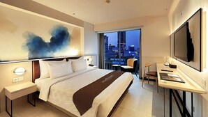 Et moderne hotelværelse med en stor seng, et skrivebord, en stol, et fjernsyn og udsigt over byen.