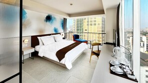 Et moderne hotelværelse med en stor seng, en balkon med udsigt over byen, et skrivebord med kaffemaskine og et fjernsyn.
