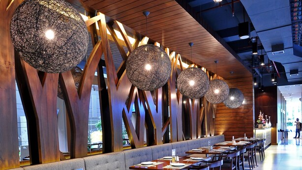 En moderne restaurant med trædetaljer og usædvanlige, sfæriske lamper. Bordene er pænt anrettet med stole.