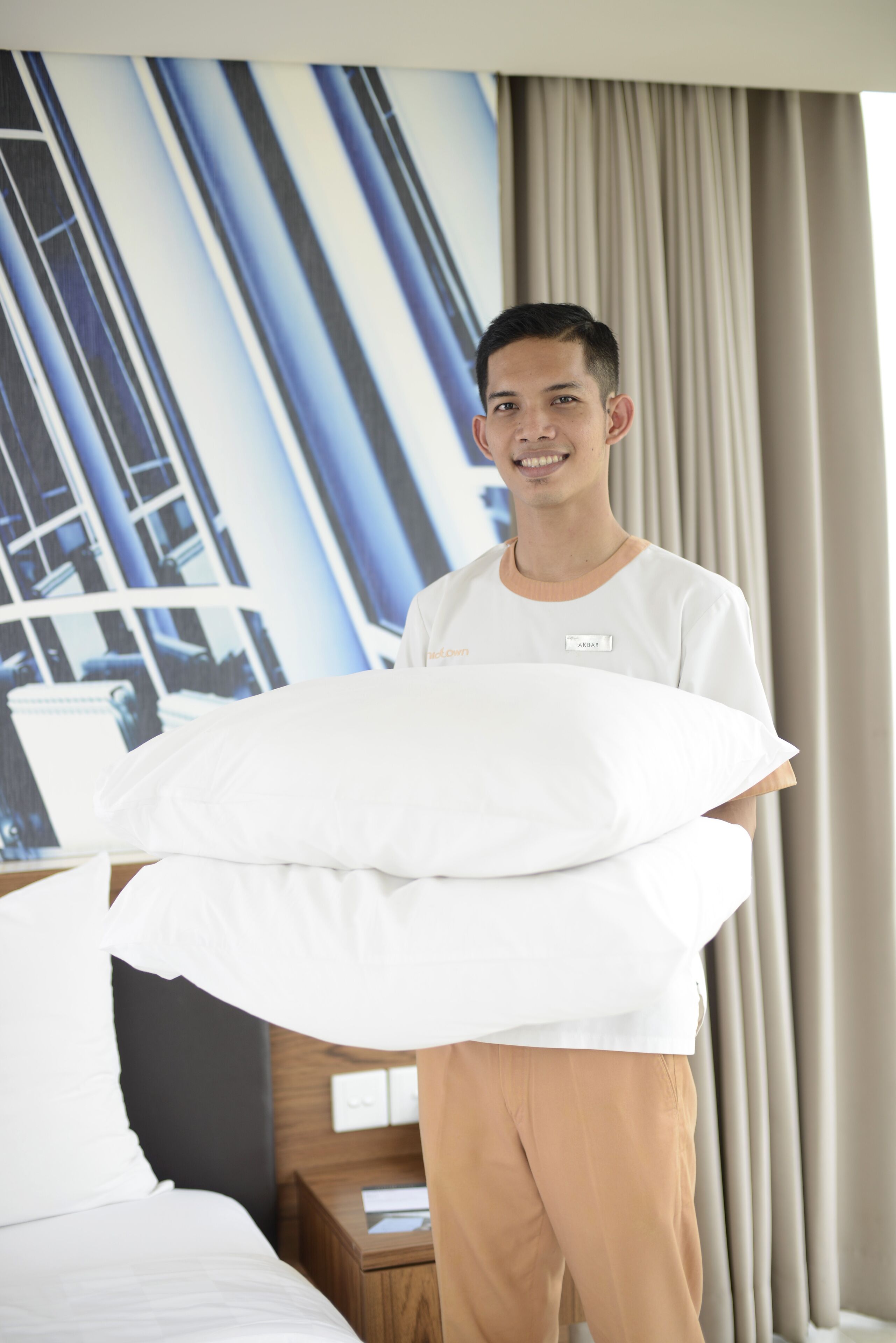A hotel room with a bed, a nightstand, and a large window with curtains.