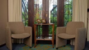 Two armchairs facing each other with a small wooden table between them, a patterned rug on the floor, and a window with curtains and greenery outside. - Susana Just B&B (Florida)