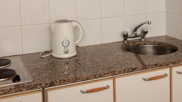 A kitchen with a granite countertop, a white electric kettle, a stainless steel sink, and a built-in stove. - Susana Just B&B (Florida)