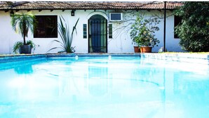 A swimming pool with a tiled edge, a white building with a tiled roof, and potted plants. - Susana Just B&B (Florida)