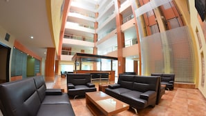 A spacious lobby with multiple black leather sofas, a wooden coffee table, and a high ceiling with glass railings. - Hostalia Hotel Expo & Business Class (Guadalajara)
