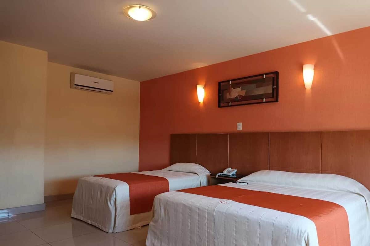 Ein Hotelzimmer mit zwei Betten, einer Deckenleuchte, einer Klimaanlage und einem gerahmten Bild an der Wand.