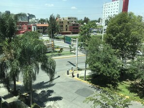 A parking area with a pedestrian crossing, surrounded by palm trees and buildings in the background. - Hostalia Hotel Expo & Business Class (Guadalajara)