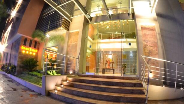 A hotel entrance with a glass facade, a set of outdoor stairs, and a well-lit reception area. - Hostalia Hotel Expo & Business Class (Guadalajara)