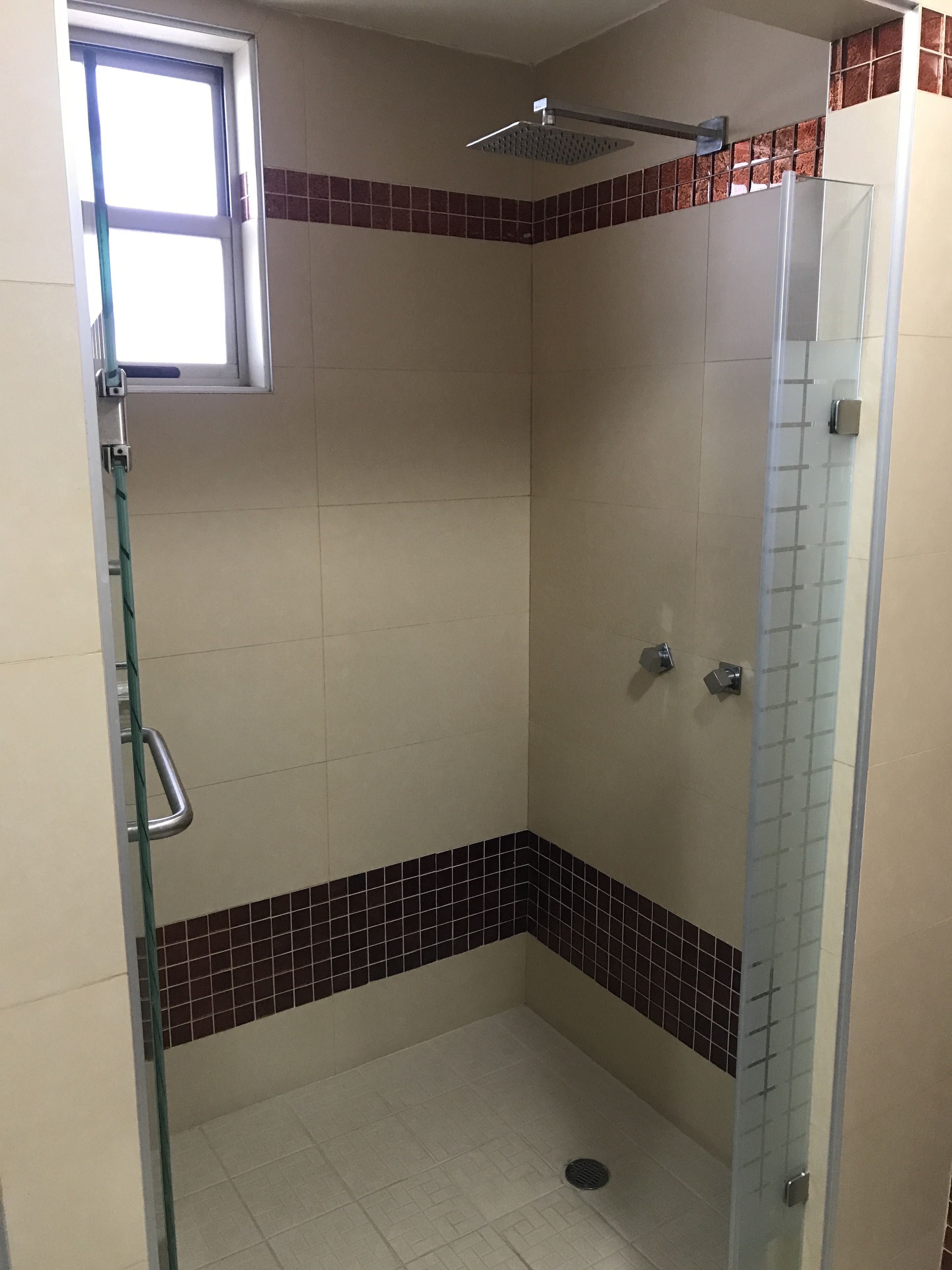 A small, enclosed shower area with a glass door, a window, and a tiled floor.