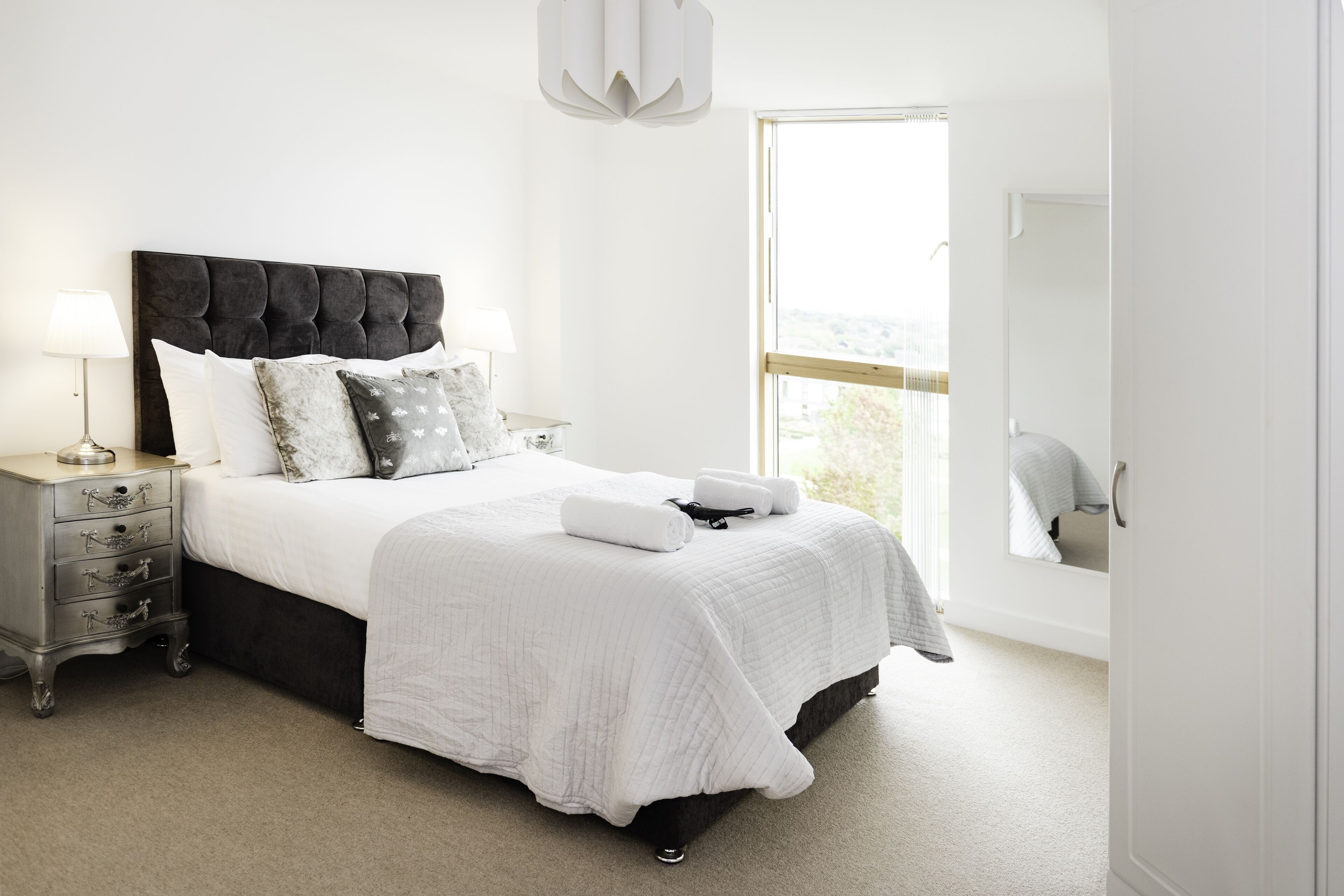 A bedroom with a large bed, bedside tables, a nightstand, a window with a view, and a mirror.
