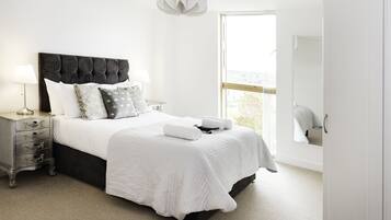 A bedroom with a large bed, bedside tables, a nightstand, a window with a view, and a mirror.