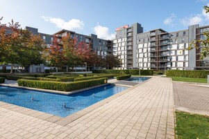 Un edificio residencial moderno con piscina, setos bien recortados y un camino pavimentado.