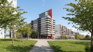 Un bâtiment moderne à plusieurs étages, avec une partie rouge bien visible et un chemin piétonnier pavé qui y mène.